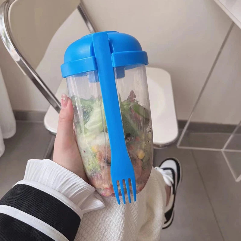 Hand holding a blue lid and fork with a salad inside a container on a bathroom floor.