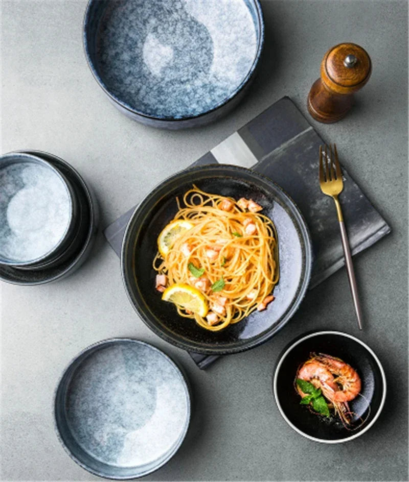 Dinner setting with pasta dish, shrimp, and empty bowls on a gray surface.