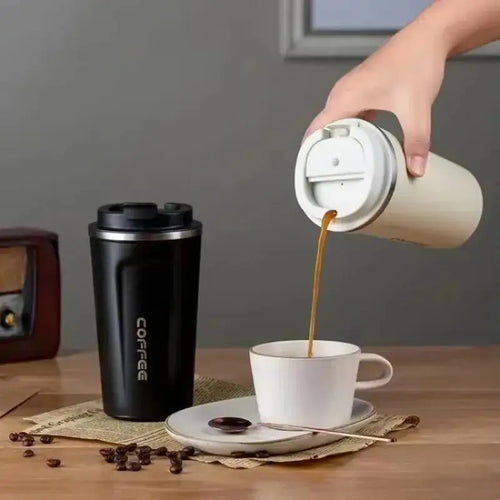 Hand pouring coffee from a beige travel mug into a white cup on a wooden table.