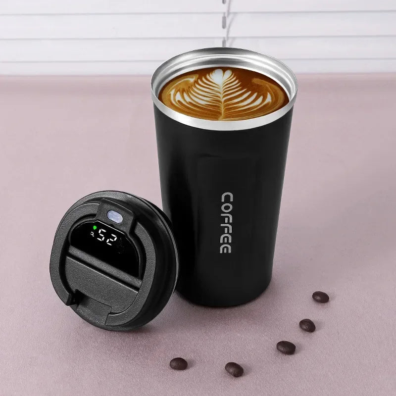 Black insulated coffee tumbler with a lid, filled with coffee, on a light pink surface with coffee beans.