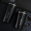 Two black coffee tumblers with 'coffee' text on a dark surface with scattered coffee beans.