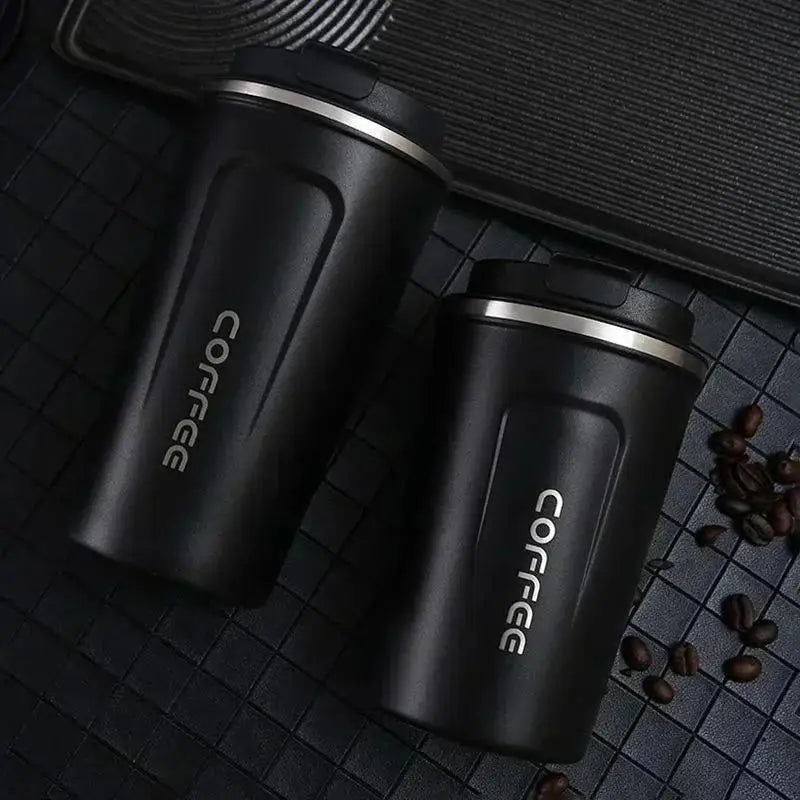 Two black coffee tumblers with 'coffee' text on a dark surface with scattered coffee beans.
