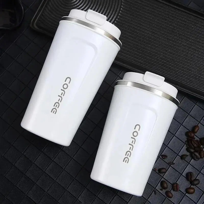 Two white coffee tumblers with silver lids on a dark surface with coffee beans.