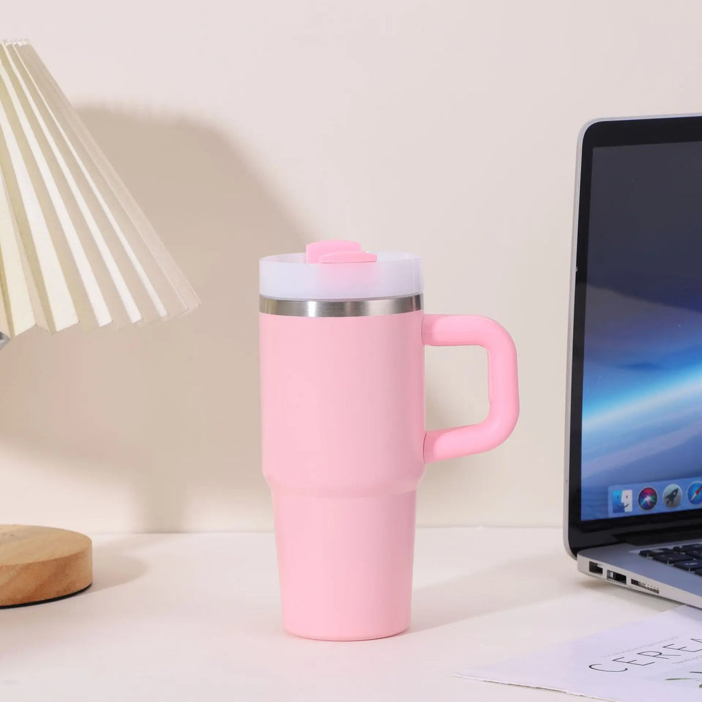 Pink insulated mug with handle on a desk next to a laptop