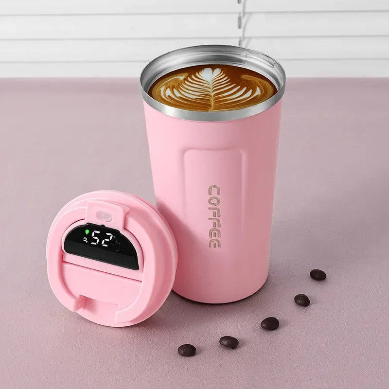 Pink insulated coffee tumbler with digital temperature display on a pink surface with coffee beans.
