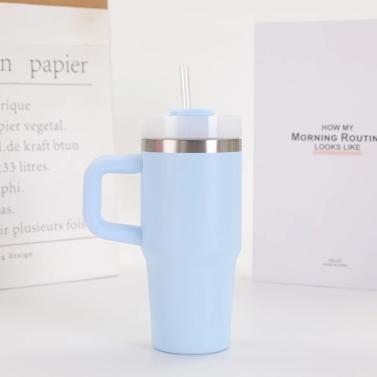 Light blue insulated mug with a straw lid on a white surface with books in the background