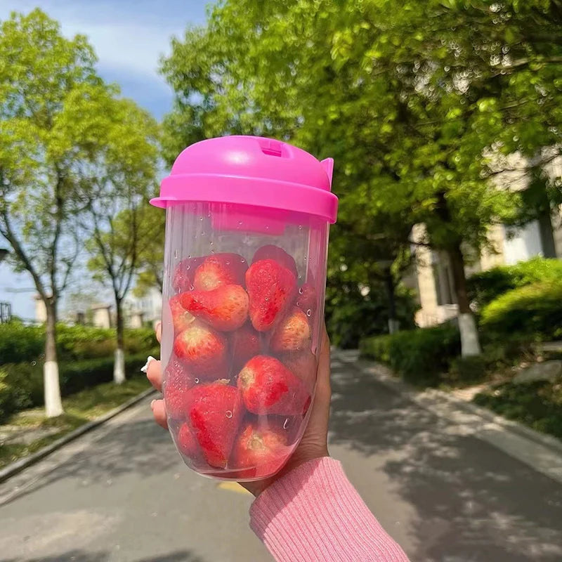 Hand holding a pink tumbler filled with strawberries outdoors.