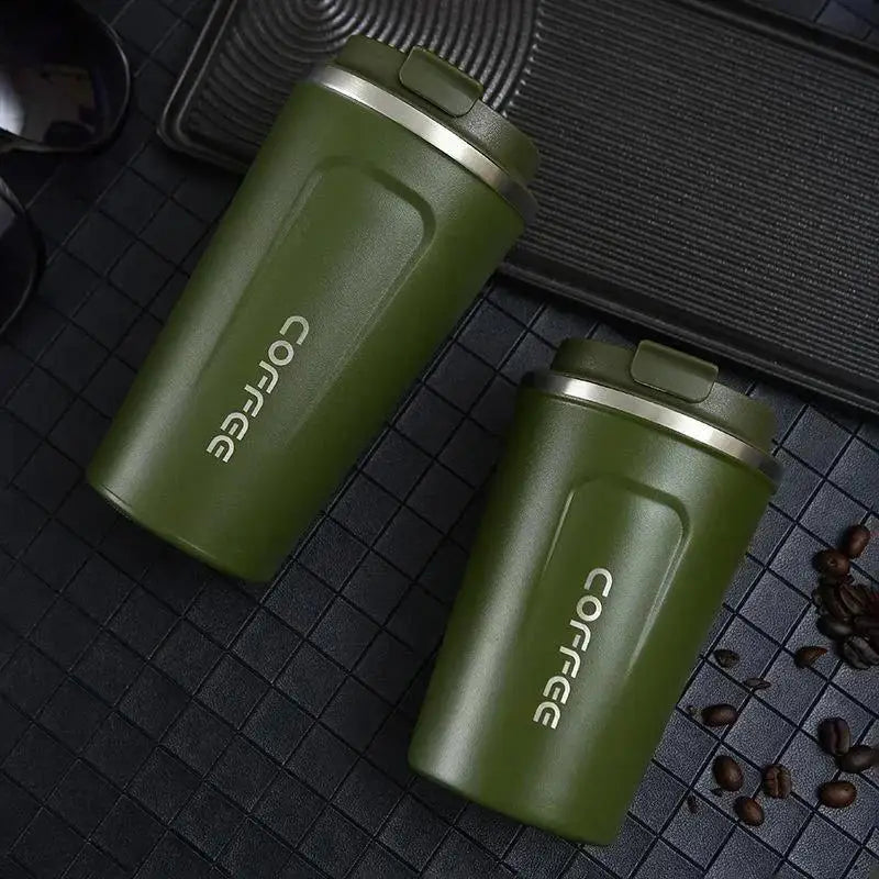 Two green coffee tumblers with 'COFFEE' branding on a dark surface with scattered coffee beans.