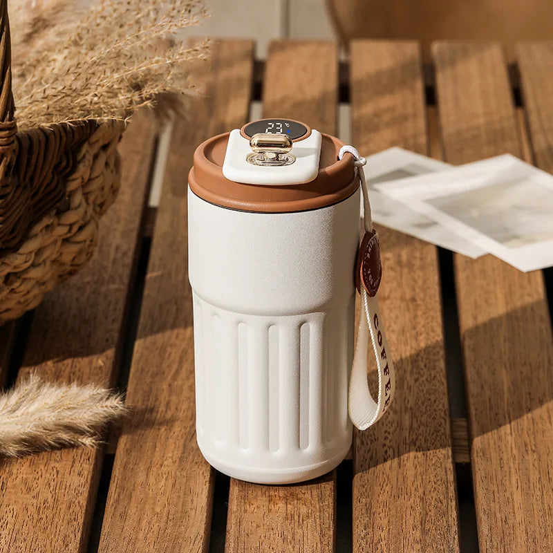 White and brown travel mug on a wooden surface with a basket and paper towel in the background.