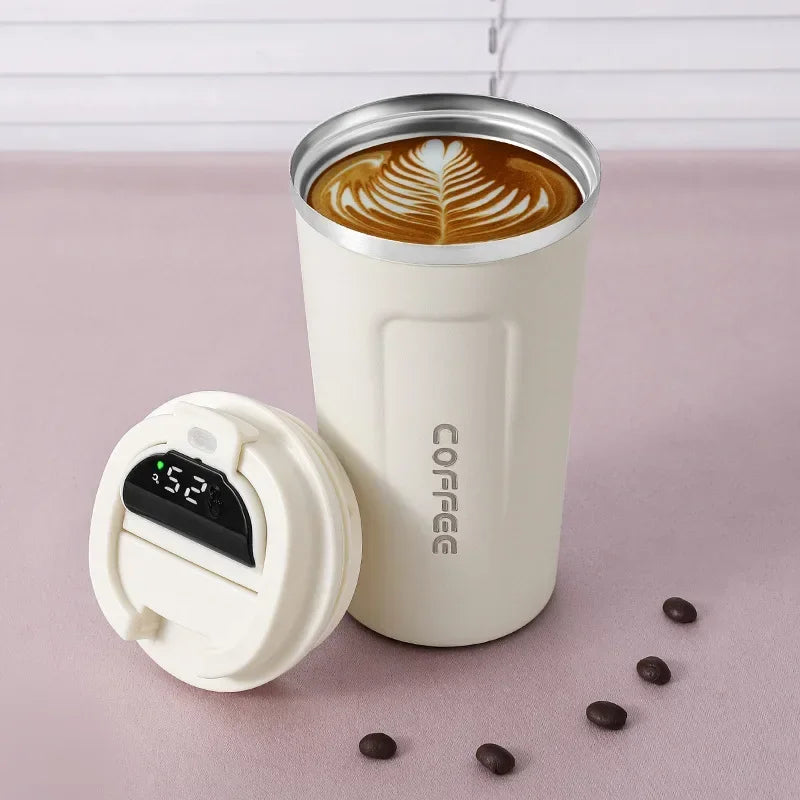 White insulated coffee tumbler with a digital temperature display on a pink surface with coffee beans.