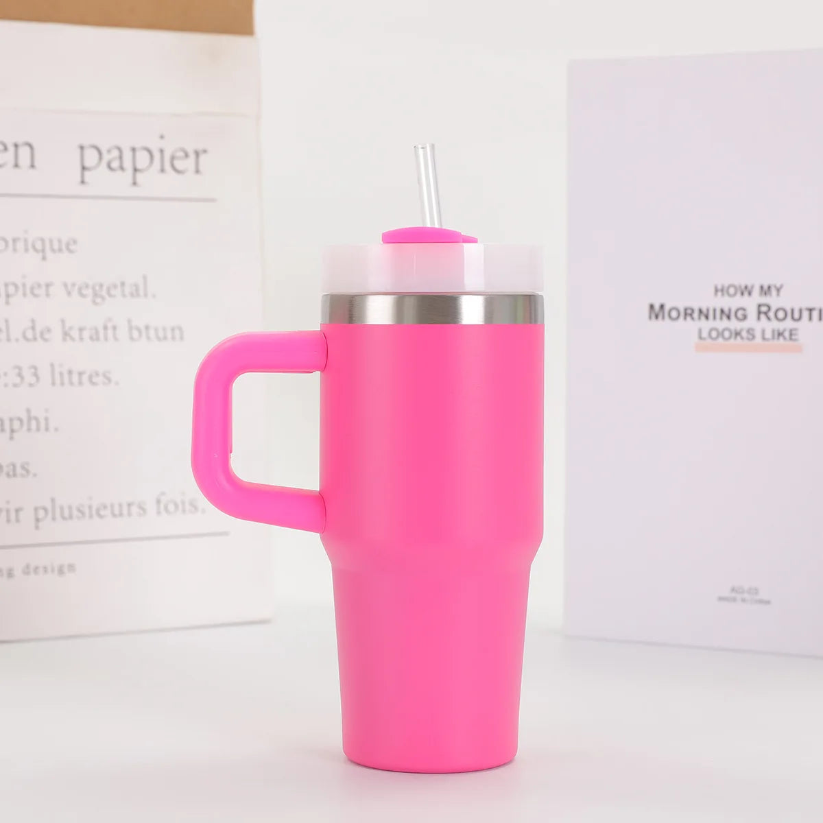 Pink insulated mug with a handle and straw lid on a white surface.