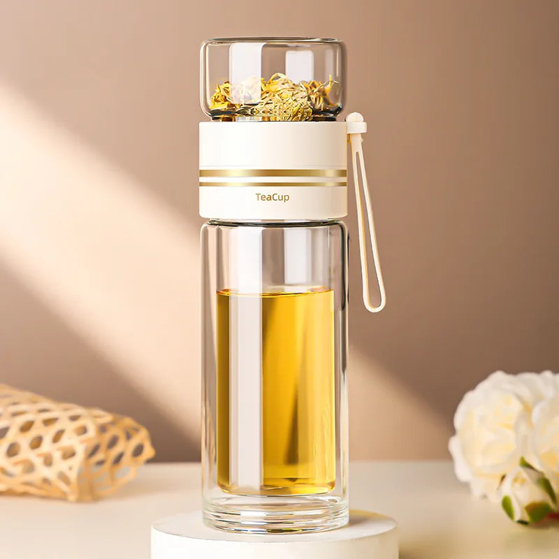 Clear glass tea infuser bottle with gold accents on a beige background