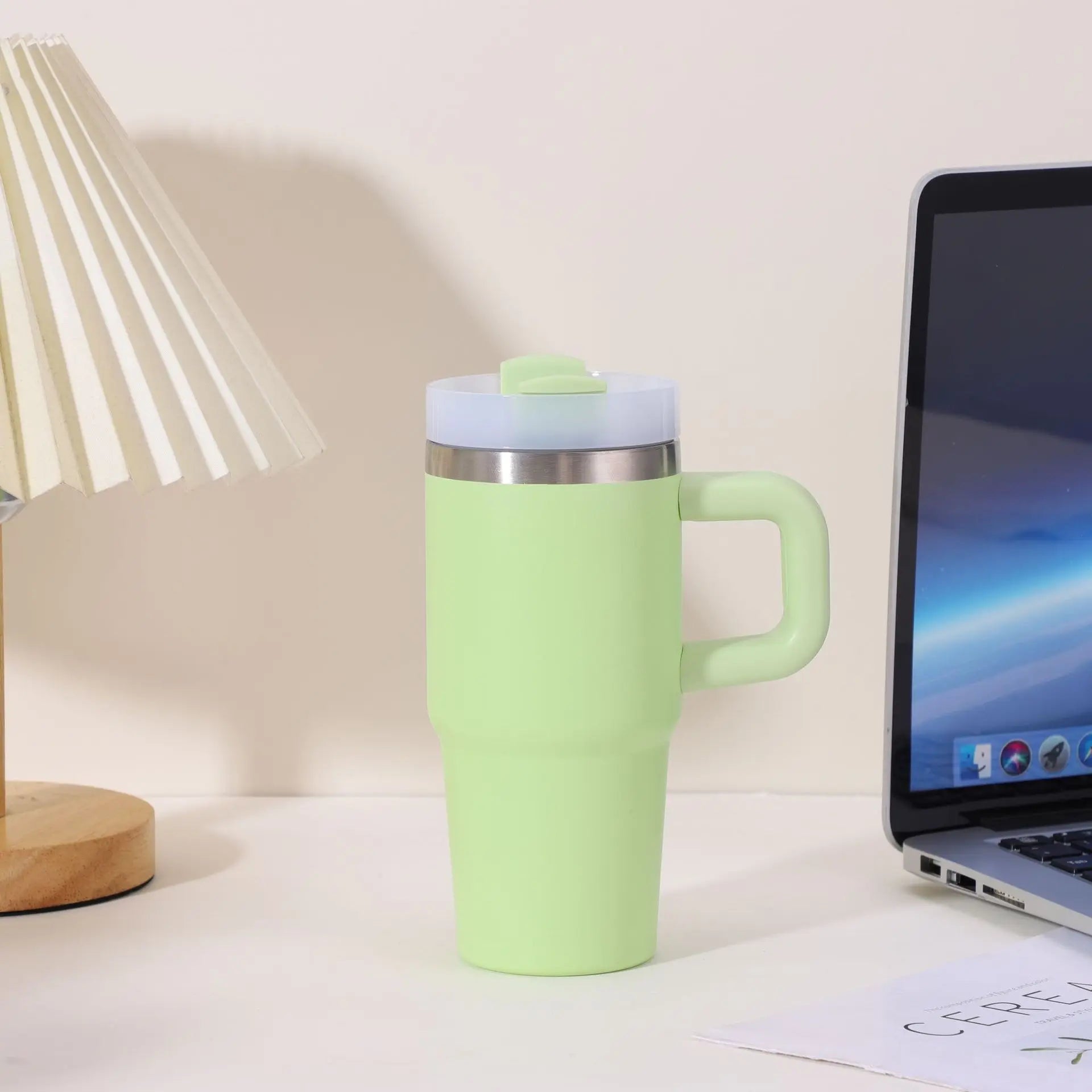 Green travel mug on a desk with a laptop and lamp in the background
